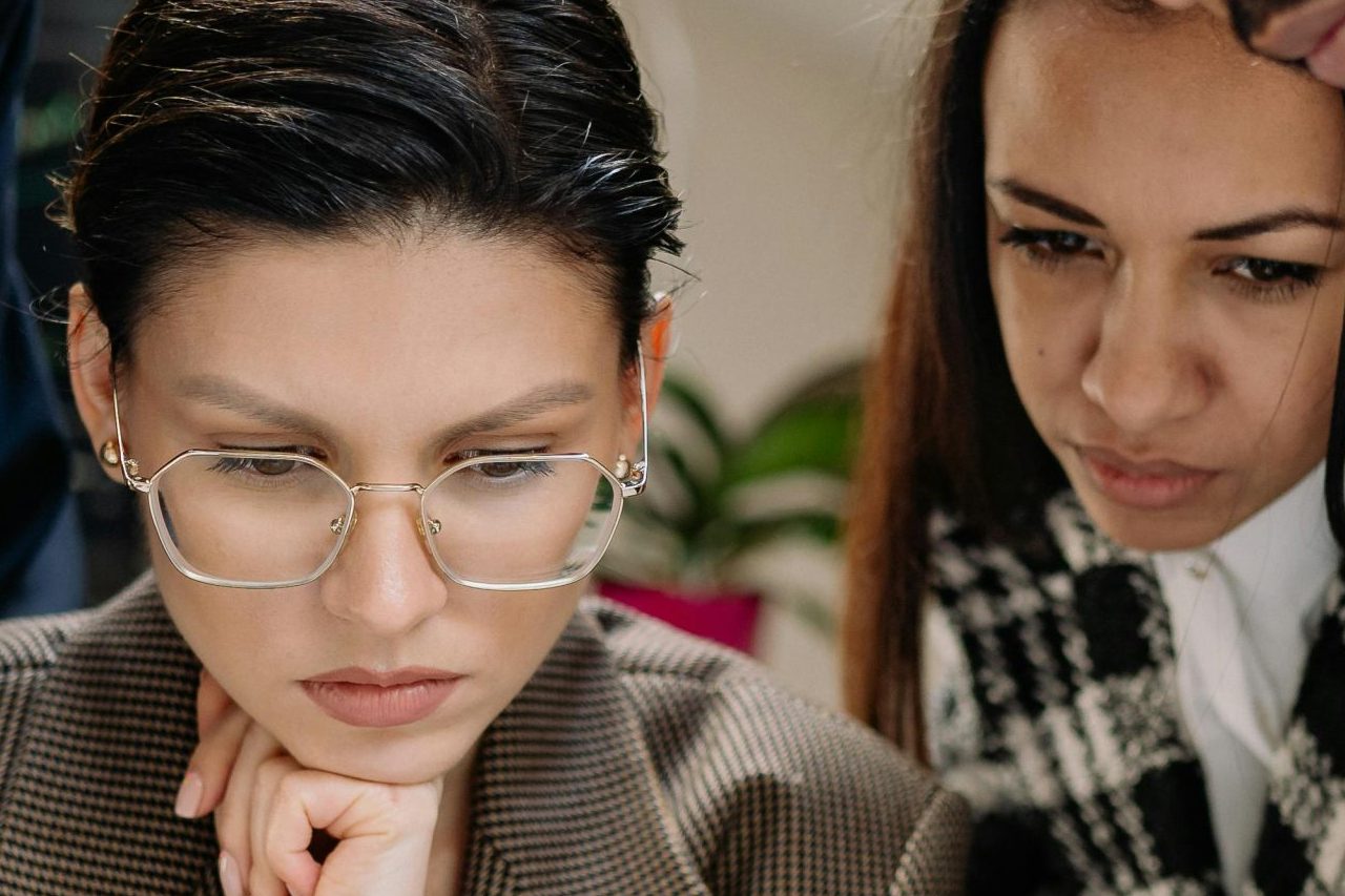 A diverse group of professionals intensely collaborating over a laptop indoors.